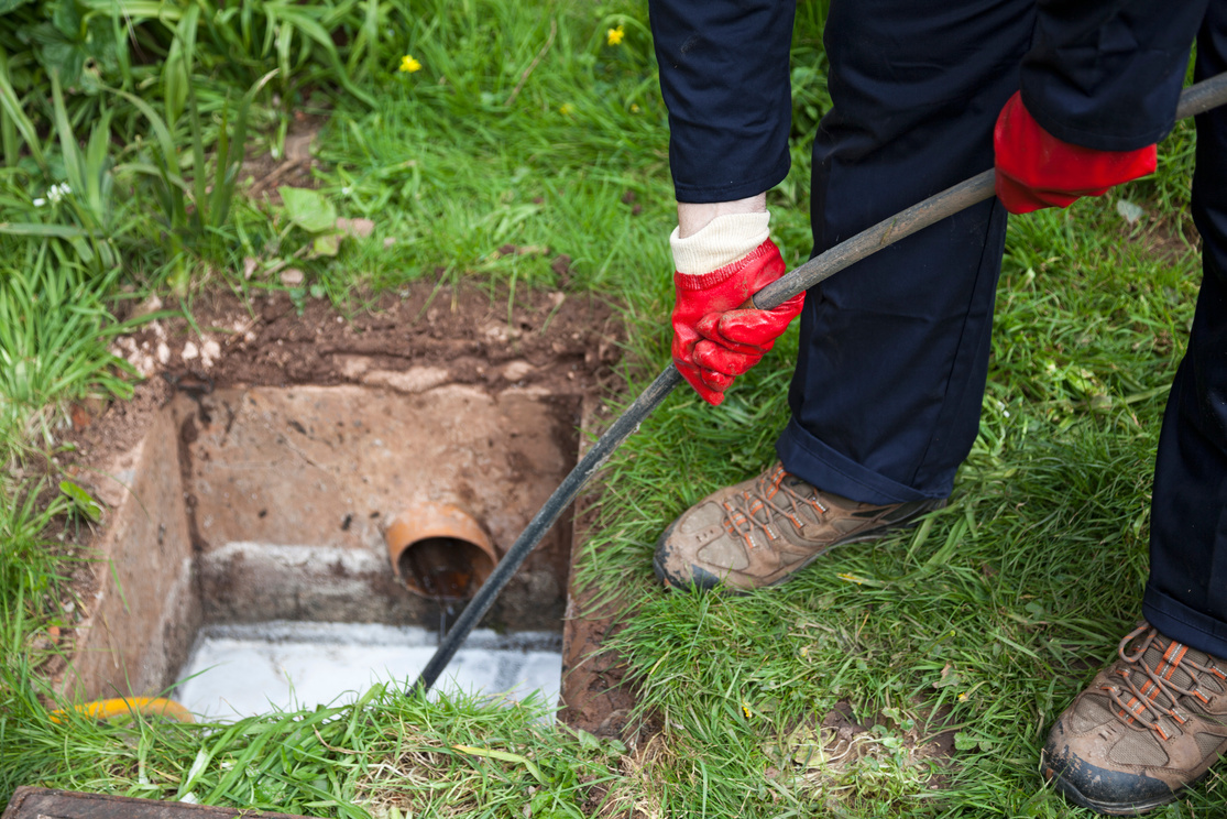 Man with ground open unblocking a drain with a tool